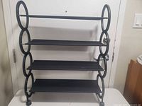 Metal shoe rack with four shelves and circular side supports, photographed against a white door.