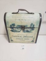 External front view showing weathered box design, vintage text and illustration, clasp lock and leather handle.