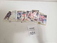 Photo of a spread of 22 vintage hockey cards laid out horizontally on a white surface, showcasing various players in different colored uniforms from past decades, very good condition visible.