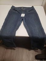 Front view of a single pair of blue denim jeans laid flat, showing the full length and general condition.