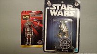 Photo showing two new Star Wars droid figures in original packaging: metal keychain figure and R2-D2 figure.