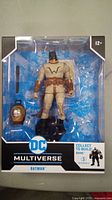 Photo shows DC Multiverse Batman action figure in packaging with accessories and extra head visible.