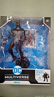 DC Multiverse Omega action figure in original packaging showing figure and accessory figure, box displays branding and recommended age 12+.