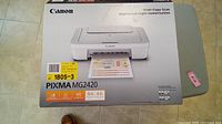 Box showing Canon PIXMA MG2420 all-in-one printer image and specifications, printer appears new, toner/ink status unknown