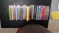 Photo showing 27 assorted music CDs arranged side-by-side on a black table surface.