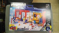 Photo shows a sealed Playmobil NHL hockey play set box with colorful graphics depicting a small hockey rink, players, and accessories. The box states 71 pieces and is suitable for children aged 5 and up.