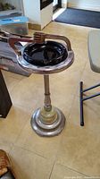 Full view of vintage standing ashtray showing metal frame, black ashtray bowl, ornate stem, and stable base.