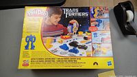 Box front showing a child playing with the Transformers Play-Doh kit including the blue robot mold and various tools.