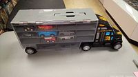Photo showing black and grey toy truck with trailer open revealing six small toy cars inside compartments.