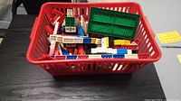 Red basket containing assorted vintage LEGO bricks and plates including a large green baseplate.
