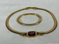 Gold tone Swarovski choker with central colored stones and Swarovski hinged bangle side by side on white cloth.