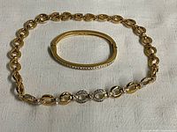 Two-piece set: a gold-tone Swarovski choker necklace with crystal accents, paired with a gold-tone hinged Swarovski bangle featuring crystal detailing on top, displayed on white fabric.