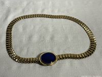 Full view of the brass belt laid out flat showing the chain-link design and the large cobalt blue glass stone centerpiece.