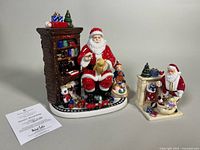 Two Royal Doulton Christmas porcelain figurines depicting Santa Claus with detailed holiday scenes and assorted toys.