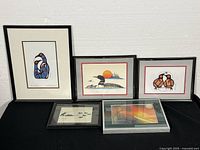 Five framed works displayed on black cloth against white background: three at back and two in front