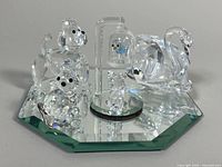 Photo of four Swarovski crystal figurines on an octagonal mirror base: two small dogs, a small bird under glass dome, and a swan.