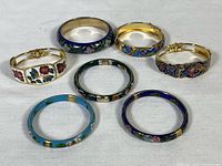 Top down view of seven cloisonné brass bangles arranged on a white cloth background