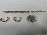 Full lot of three Swarovski jewelry items: gold-tone bracelet, gold-tone earrings, silver-toned flower brooch on white cloth.
