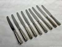 Full view of all nine Birks dinner knives arranged side-by-side showing polished blades and sterling silver handles.