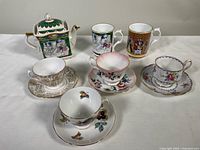 Full lot showing one square Hamlet-themed Sadler bone china teapot, four assorted teacups with matching saucers and three illustrated mugs.