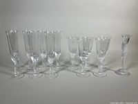 Full set of 13 pieces including 7 tagged glasses, 5 signed glasses, plus one signed candleholder, arranged in a single line on white background.