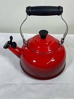 Red Le Creuset enamel-on-metal whistling kettle with black handle and lid knob, side view.