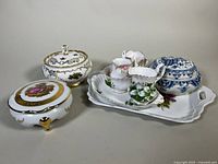Shows overall lot: Royal Albert cream and sugar set on a rectangular under-plate with floral decoration; blue and white covered dish; two covered trinket boxes, one with floral gold design and another with pink rose painting.