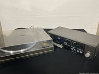 Photo showing turntable with clear plastic dust cover and stereo cassette deck side by side on a surface.