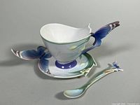 Full view of the teacup on saucer with matching spoon placed beside them on a gray surface.