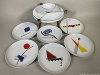 Six 9.5 inch white porcelain plates, each with different colorful abstract geometric design, arranged in a semicircle