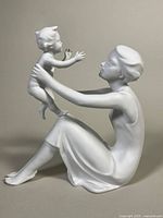 Side view of the white bisque porcelain figurine showing a seated woman reaching out to a standing child, capturing the detailed facial expressions and posture.