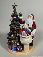 Front view of the Royal Doulton Santa figurine next to a decorated Christmas tree with gifts and toys.