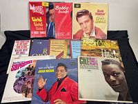 Full view of all nine vinyl record albums laid out on a dark cloth. Visible albums include Elvis Presley 'Girls! Girls! Girls!', 'King Creole', Bobby Swings, Freddy Cannon Greatest Hits, Jackie Wilson 'Higher and Higher', The Supremes, and others.