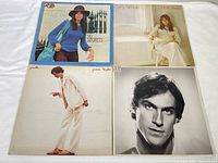 Four vinyl record album covers laid out on white fabric showing two albums by James Taylor and two by Carly Simon