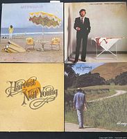 Four vinyl record album covers - Neil Young's 'On the Beach,' Eric Clapton's 'Money and Cigarettes,' Neil Young's 'Harvest,' and Neil Young's 'Old Ways' arranged in a square layout on a wood floor.