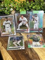 Five baseball cards displayed on a brown wooden surface with greenery in the background, showing players Victor Acosta, Blaze Jordan, Jasson Bello, and Bobby Witt Jr.