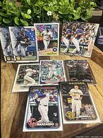 Photo of 10 rookie baseball cards arranged on a wooden surface with green plants in the background, showing players including Oneil Cruz, Yordan Álvarez, Merril Kelly, Kyle Manzardo, and others.