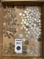 Overall view of multiple coins arranged in a cardboard box, showing a variety of sizes and colors from different countries.