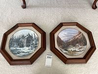 Two hexagonal wood framed collector plates showing a watermill and a mountain river valley scene.