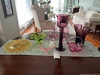 Full view of the glassware lot on a table, showing various colored glass items including yellow, green, pink, and purple pieces.