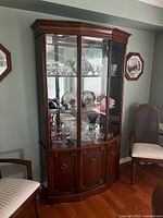 Front and angled view of Deilcraft china cabinet showing dark wood finish, glass doors, glass shelves with displayed glassware and mirrored back, and wood storage cabinets below