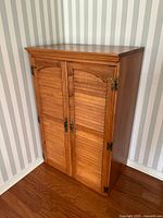 Full view of the wooden media cabinet with double doors, showing the cabinet placed against a wall and floor with wood texture.