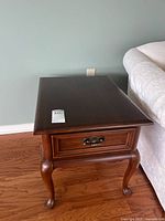 Full view of one end table showing top surface, drawer front, and cabriole legs.