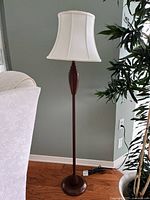 Full view of the floor lamp showing brown wooden base and stand with white fabric shade against a neutral wall and wooden floor.