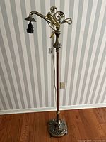Full view of the vintage metal floor lamp showing the tall ornate structure with detailed base and upper decorative arm, cord and plug visible.