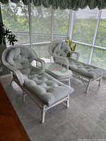 Two wicker chaise lounge chairs with tufted light green cushions and matching wicker side table with glass top