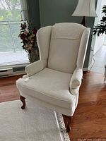 Front view of ivory wingback chair showing seat, arms, headrest cover, and legs.