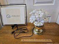 Front view of the vintage 1980s brass flower lamp on a wooden surface with ruler for scale.