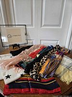 Overview of all scarves laid flat on a wooden surface with light coming from left. Includes various patterns and materials rolled out for display.