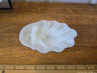 Front view of the white milk glass soap dish showing cherub and scalloped shell design, positioned on wooden surface with ruler for scale.